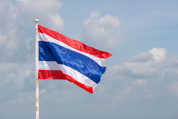 A lone Thai flag waving in the wind on a bright, sunny day, with clouds in the background.