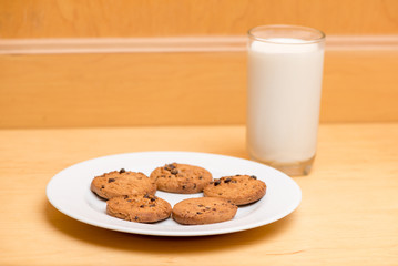 Close-up of a plate of chocolate chip cookies and a glass of milk, ready for Santa Claus to eat. Food and holidays concept.