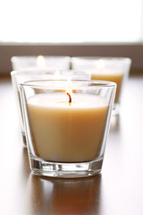 Four tan candles in glass cups with daylight streaming in through window