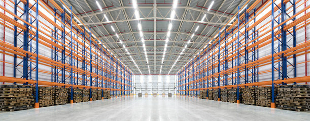 Panorama of an empty huge distribution warehouse with high shelves and pallets