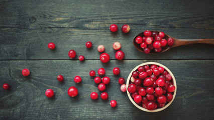 Fresh juicy cranberry in wooden round bowls with a wooden spoon on a table, top view
