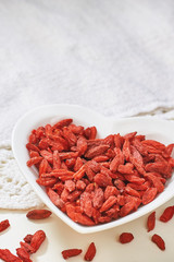 Dried goji berries in heart shaped ceramic bowl on white table. Copy space