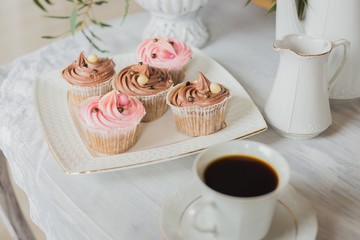 Wedding decorations zone - white table with bouquet, pink candles, cup of coffee and cupcakes, close up shot of cupcakes