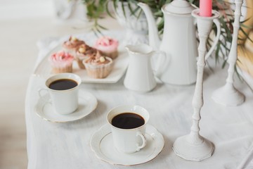 Wedding decorations zone - white table with bouquet, pink candles, cup of coffee and cupcakes