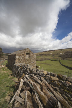 A Pile Of Wood Laying Beside A Stone Wall And A Stone Building; Swaledale, England