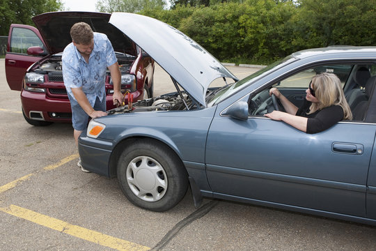 A Man Helps Boost The Car Battery Of A Woman's Car In A Parking Lot; Edmonton, Alberta, Canada