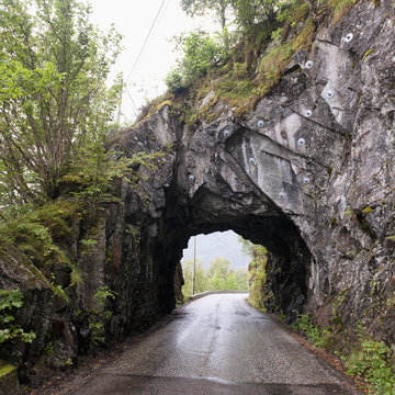 A Wet Road Leading Through A Tunnel In A Rock Cliff; Bergen, Norway