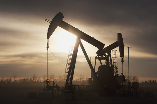 Silhouette of two pump jacks at sunrise with clouds, Alberta, Canada