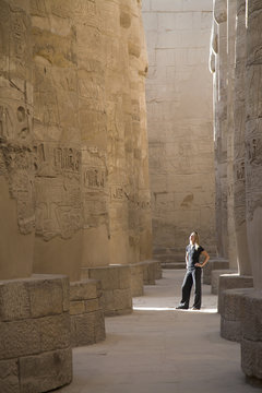 A Woman Tourist Stands At The Base Of The Massive Columns In The Temples Of Karnak On The East Bank Of Luxor Along The Nile River; Luxor, Egypt