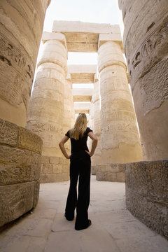 A Woman Tourist Stands At The Base Of The Massive Columns In The Temples Of Karnak On The East Bank Of Luxor Along The Nile River; Luxor, Egypt