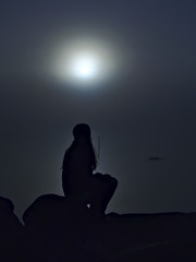 Silhouette of a woman sitting by foggy sea in moonlight.