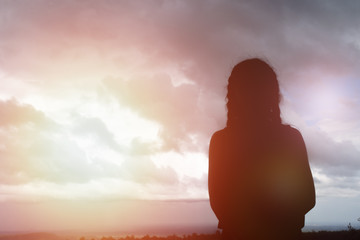 Silhouette of woman praying over beautiful sky background.