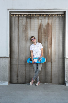 Handsome man posing with skateboard near the wall