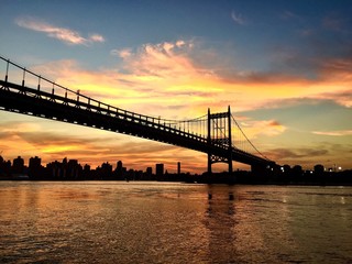 Silhouette of Triborough Bridge with sunset sky between Astoria park and buildings of Manhattan, New York
