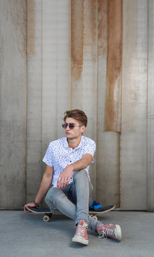 Young stylish man in sunglasses sitting on a skateboard.