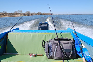 Feed motor boats. The boat leaves a trail on the water. Bag and fishing rods in the back seat