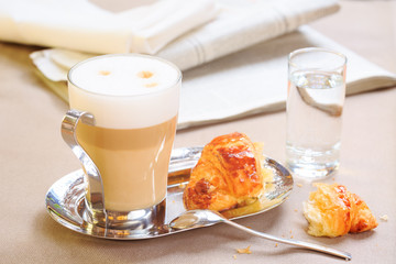 Cup of latte with croissant. Tablecloth background with newspape