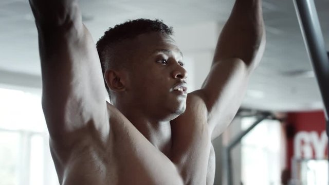 Athletic handsome male fitness model executing pull ups on horizontal bar in gym