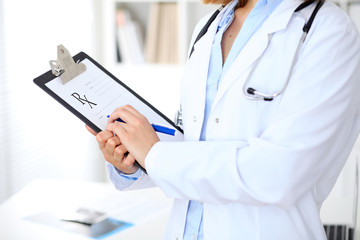 Close up of  female doctor  writing a medical prescription at clipboard while standing