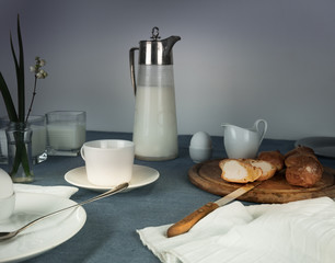 still life. rustic dinner. milk jug, candles, tea, eggs, bread rolls on the table
