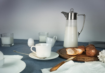 still life. rustic dinner. milk jug, candles, tea, eggs, bread rolls on the table