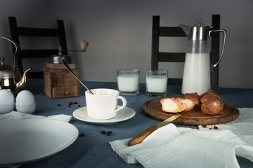 still life. rustic dinner. milk jug, candles, tea, eggs, bread rolls on the table