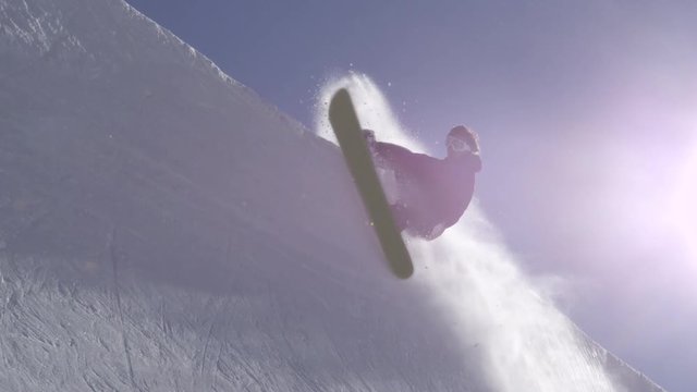 SLOW MOTION: Young pro snowboarder spraying snow in half pipe in sunny snowpark