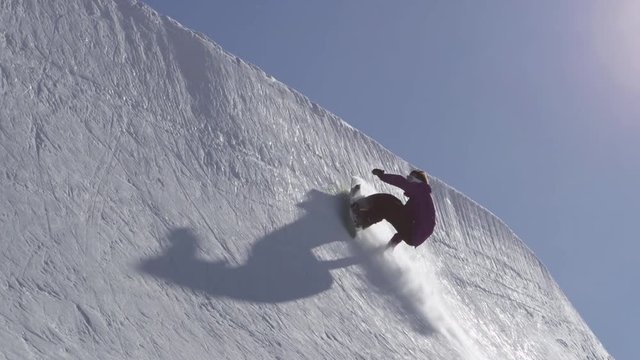 SLOW MOTION: Young pro snowboarder spraying snow in half pipe in sunny snowpark