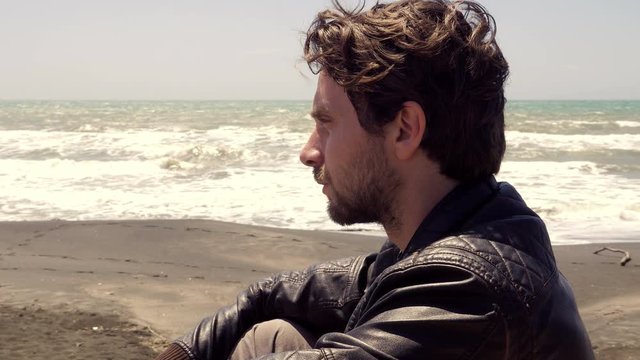 Sad lonely man sitting in front of ocean thinking dolly shot closeup