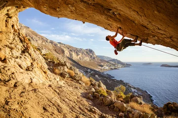 Poster Male climber on overhanging rock against beautiful view of coast below © Andrey Bandurenko