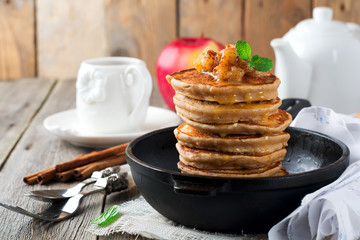 Stack of pancakes from buckwheat flour with baked apples and cinnamon on old wooden background. A healthy breakfast. Selective focus.