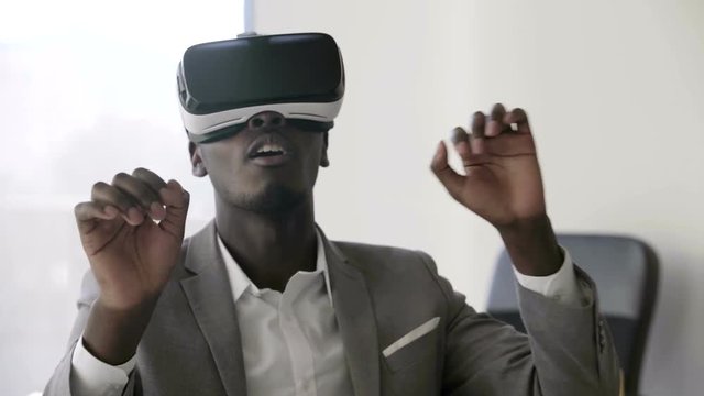 Young black man wearing virtual reality headsets in white future white office. He clicks his fingers in the air and turns his head