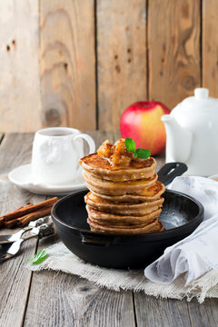 Stack of pancakes from buckwheat flour with baked apples and cinnamon on old wooden background. A healthy breakfast. Selective focus.