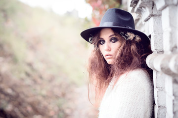 Beautiful girl on brick wall background. Girl in the hat. Gloomy makeup. Halloween. Fashionable woman. Casual wear. Trend clothing. Toned image.