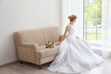 Fototapeta premium Bride in beautiful dress with wedding bouquet sitting on sofa