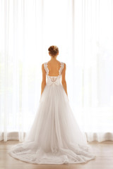 Fototapeta na wymiar Bride in a beautiful wedding dress standing near window