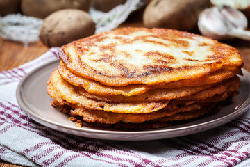 Stack of potato pancakes on a wooden table. In the background po
