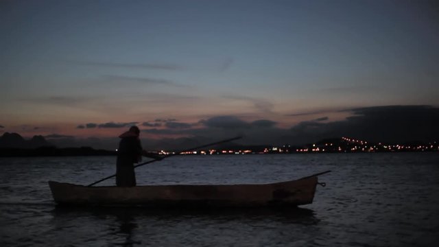 Canoeing at night, Brazilian man paddles across Imboassica lake in Rio De Janeiro at sunset, 