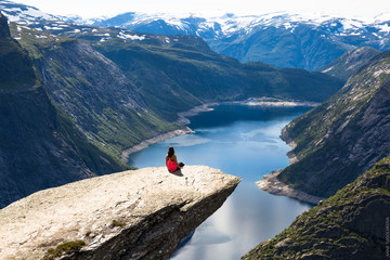 Young woman doing yoga on Trolltunga. Happy girl enjoy beautiful lake and good weather in Norway.