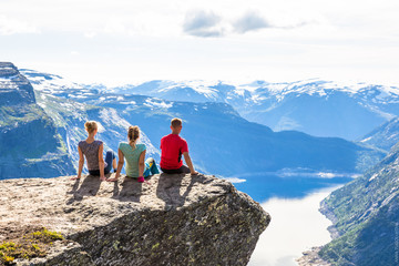 Happy friends relax on Trolltunga. People enjoy beautiful lake and good weather in Norway.