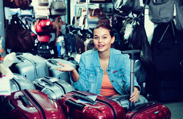 Fototapeta na wymiar Teenager girl buying large wheeled plastic luggage bag
