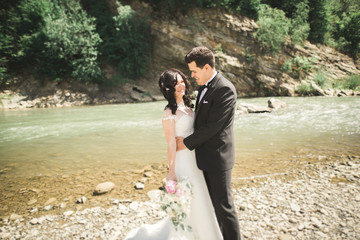 Elegant gentle stylish groom and bride near river with stones. Wedding couple in love