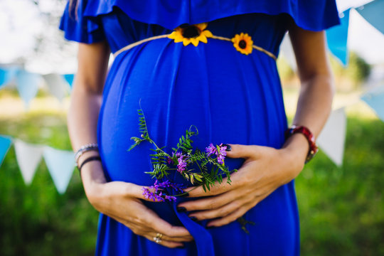 Woman in blue dress holds tiny violet flowers  under her pregnan