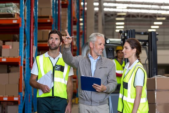 Warehouse manager and workers discussing with clipboard
