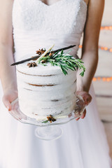 A bride holding a craft cake on a glass stand, wedding dress on the background