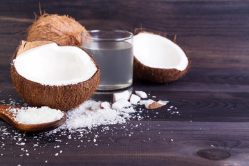 Coconut halves with shell, shavings and milk on a dark background
