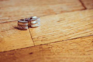 Silver cufflinks lie on wooden floor