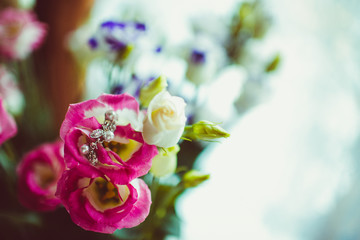 Delicate silver earrings lie over pink flower put in bouquet