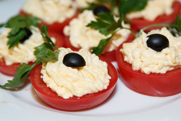 Decoration of stuffed tomatoes for eating. Food vegetable on the plate. Tomatoes with cream and black olives. Cold snack lunch.