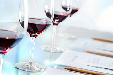 Glasses of red wine on table with pencils and paper.